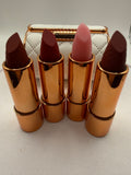Four lipsticks in gold-tone tubes displayed in front of a white quilted-style case