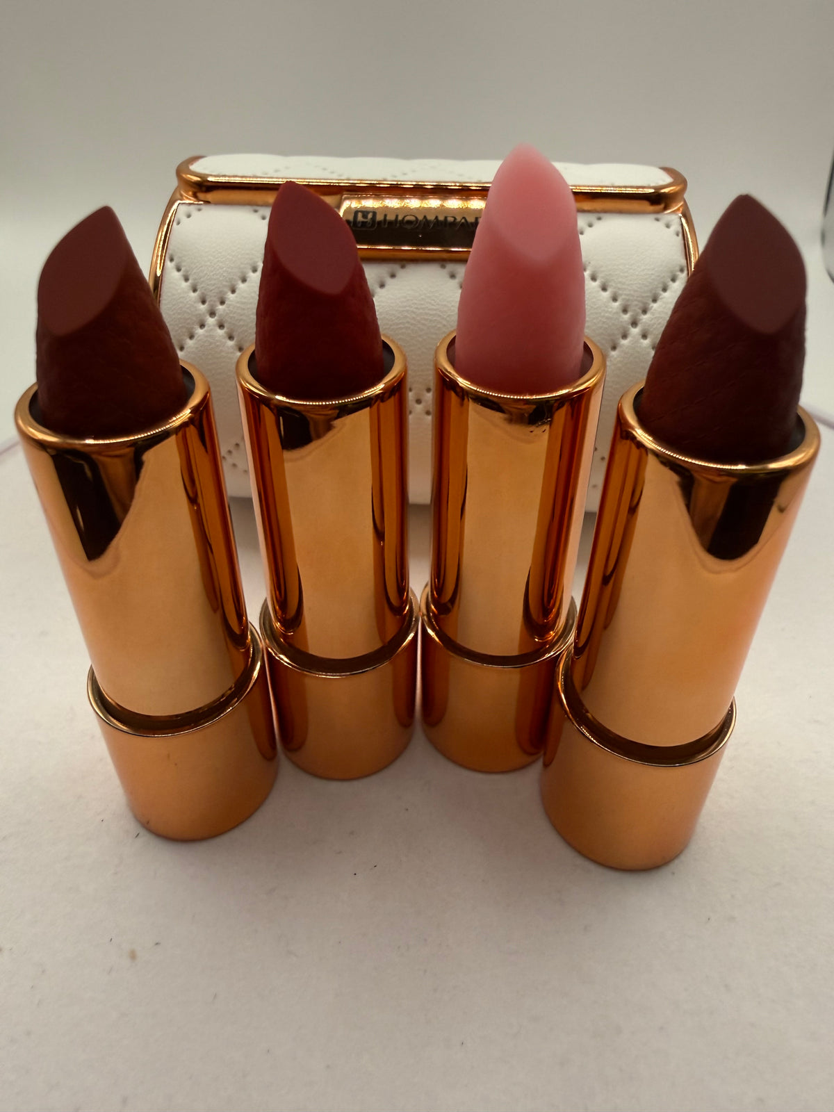 Four lipsticks in gold-tone tubes displayed in front of a white quilted-style case